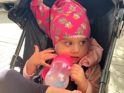 girl wearing a pink pineapple nillynoggin getting an eeg and drinking from a sipping cup while sitting in her stroller