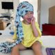 boy sitting on hospital bed getting eeg wearing a blue nillynoggin eeg cap and laughing