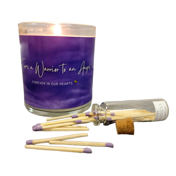 lit candle with purple label with the phrase From a Warrior to an Angel, Forever in our Hearts and a bottle of purple tipped matches