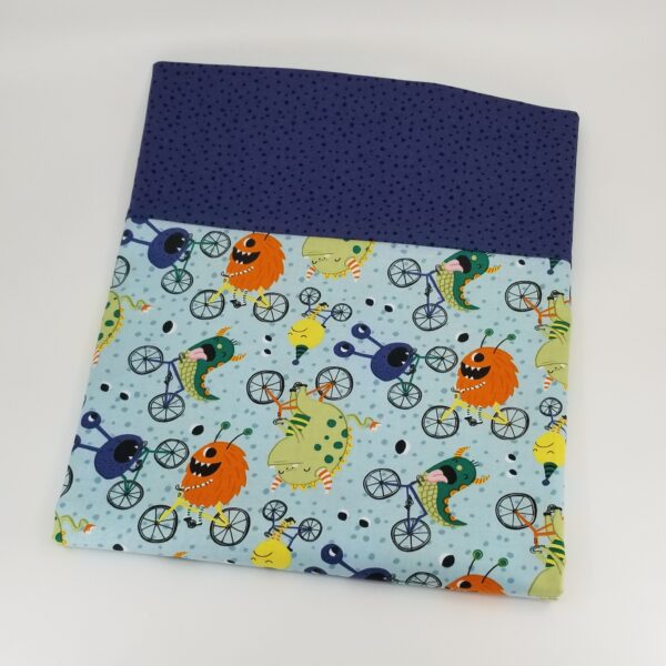 Pillowcase with pattern of silly monsters riding bicycles, light blue background, dark purple dot border
