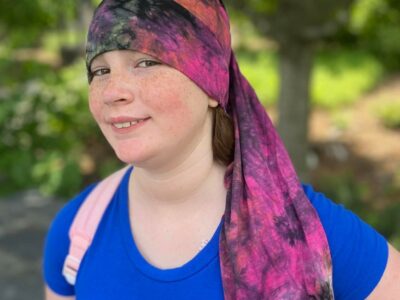 girl standing in front of trees wearing a tie dye nillynoggin eeg cap while testing for an eeg