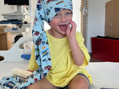 boy sitting on hospital bed getting eeg wearing a blue nillynoggin eeg cap and laughing